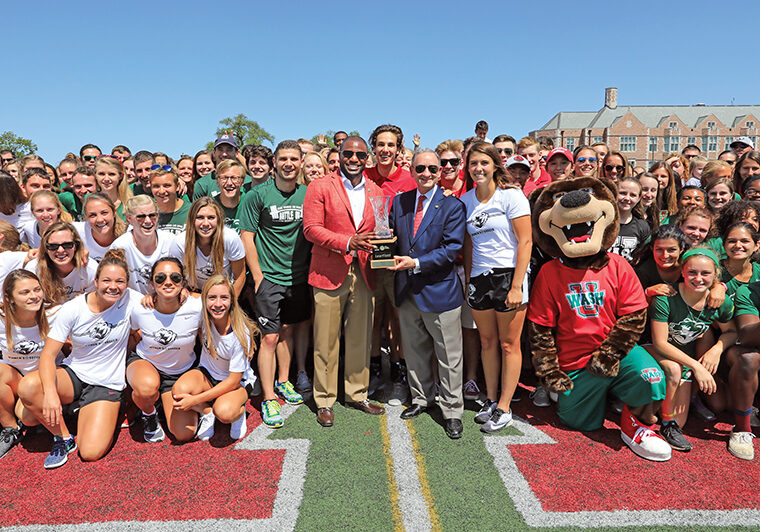 On Sept. 2, 2017, Anthony J. Azama, the John M. Schael Director of Athletics, and Chancellor Wrighton recognized all student-athletes from the previous year during halftime of a football game — an annual fall ritual. In turn, the athletes presented the chancellor with the trophy for WashU’s second-place ­finish in the Division III Learfield Directors’ Cup standings. (James Byard/WUSTL Photos)
