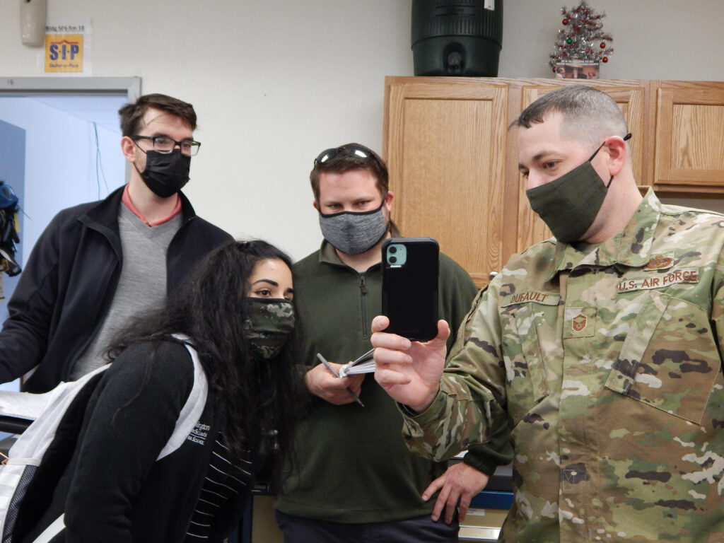 Master Sgt. Joseph Dufault, superintendent, Aircrew Flight Equipment, 375th Operations Support Squadron shows a video on his phone of the August 12, 2020, flooding of the AFE office to graduate students (left to right) Kyle Collier, Astha Bhatnagar, and Cam Loyet. The students are helping Scott’s Elevate innovation team to find potential solutions to prevent future flooding. (Photo: Courtesy of Christine Spargur)