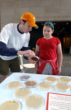 Luke Starnes, graduate student in medicine and a member of the Young Scientist Program, talks with Ellen Wright about micro-organisms, in the lobby of the McDonnell Sciences Building.