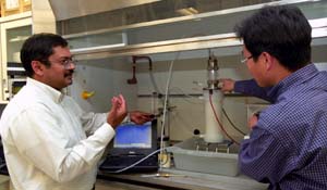Pratim Biswas, Ph.D. (left), and M.H. Lee, Ph.D., postdoctoral fellow in environmental engineering, discuss the nanostructured titanium dioxide reactor, which degrades the pollutant MTBE. Biswas discovered that a nanostructured form of titanium dioxide causes MTBE to react with dissolved oxygen so that it yields the harmless gas carbon dioxide.