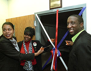 Rebel Saffold (right) of WUSTL's Association of Information Technology Professionals cuts the ribbon during the dedication of the Andrea M. Smith Technology Center at Barbara C. Jordan Elementary School Feb. 21. Helping are Anna Hollins (left), sister of Andrea Smith, and school Principal Sandra Bell.