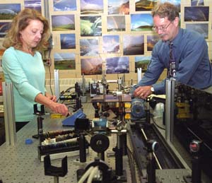 Christine  Kirmaier (left) and Dewey Holten making adjustments in their sophisticated laser laboratory in  Louderman Hall .  The husband-wife team have tricked electrons to choose another path in a bacteria's reaction center protein, the factory for photo