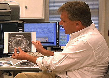 Frank J. Stadermann, Ph.D., holds an image of one of the Stardust impact craters. Though not the crater where Stadermann's team found the stardust particle, it is a fairly typical impact crater.