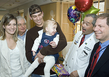 Kaidence Oliver, 22 months, shares a smile with William Chapman, M.D., at a party in her honor for being the 1,000th recipient in the University's liver transplant program. Kaidence had a liver transplant one year ago at St. Louis Children's Hospital after being diagnosed in utero with an inherited liver disease. When Kaidence and her family traveled from their home in Redbud, Ark., to the medical center Jan. 17 for her one-year checkup, she was treated to a Dora the Explorer cake, balloons and introduction to what life would be like as a movie star. Every TV station in St. Louis was on hand to capture the event. Kaidence delivered a command performance and delighted the crowd by taking several swipes of icing every time she passed the cake. With Kaidence are her parents and members of the transplant team. From left are her mother, Amber Oliver; Ross Shepherd, M.D.; her father, Matt Oliver; Chapman; and Jeffrey Lowell, M.D.