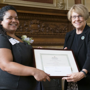 two women stand with a framed certificate