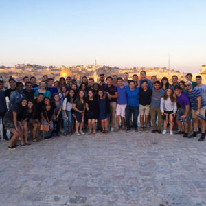 A large group of students stands together in front of the Dome of the Rock at evening