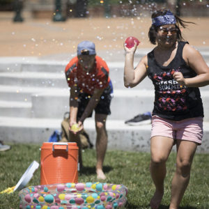 two students hold water balloons ready to toss as they get sprayed with water