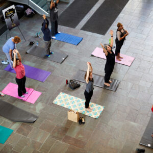 Men and women stand on yoga mats stretching.