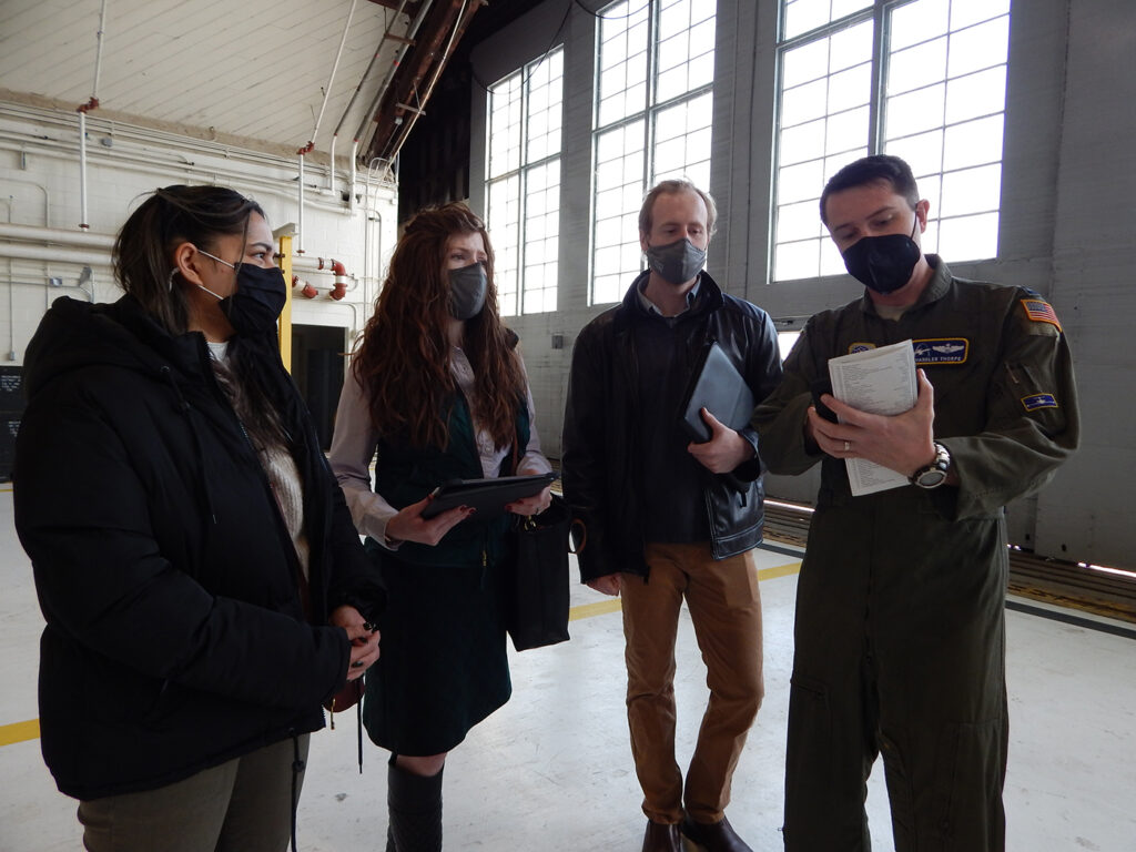 C-21 pilot Capt. Chandler Thorpe, 458th Airlift Squadron, shows Washington University graduate students (left to right) Mehir Walia, Kelsey Giaimo, and Kyle Gero a pre-flight checklist. As part of the university’s Innovation for Defense Course, the students are working with Scott Air Force Base’s Elevate innovation team and the squadron to identify potential solutions that would resolve the current challenges C-21 pilots face training on a simulator that does not match the current, updated cockpit configuration. (Photo: Courtesy of Christine Spargur)