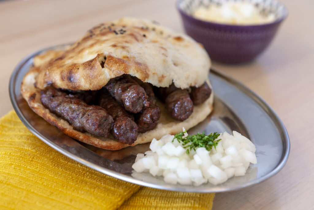 cevapi sausages in a pita on a silver plate with side of diced onions