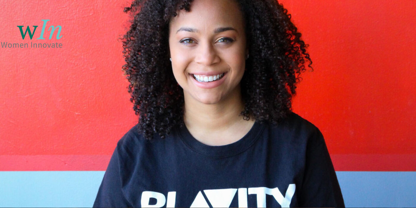 Morgan DeBaun smiles in front of a blue and red background, sporting a Blavity shirt.