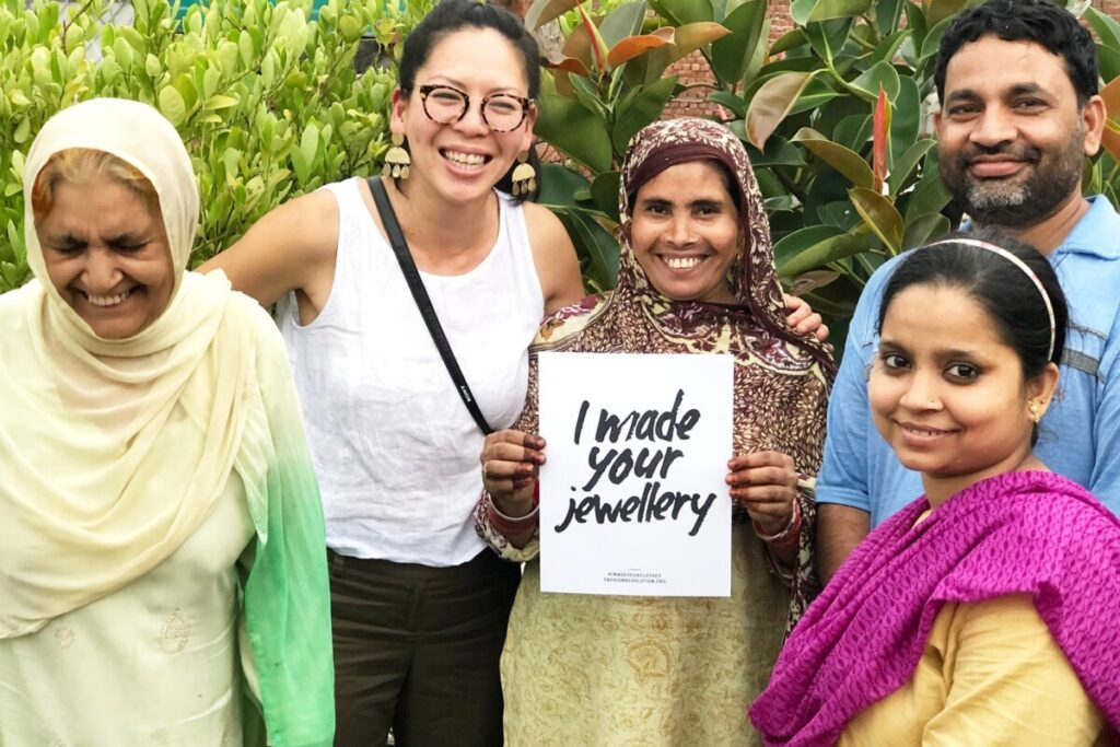 Group of south asian people standing in front of plants with sign that says "I made your jewelery"