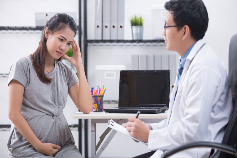 Image of a pregnant woman, looking sad, talking to a physician