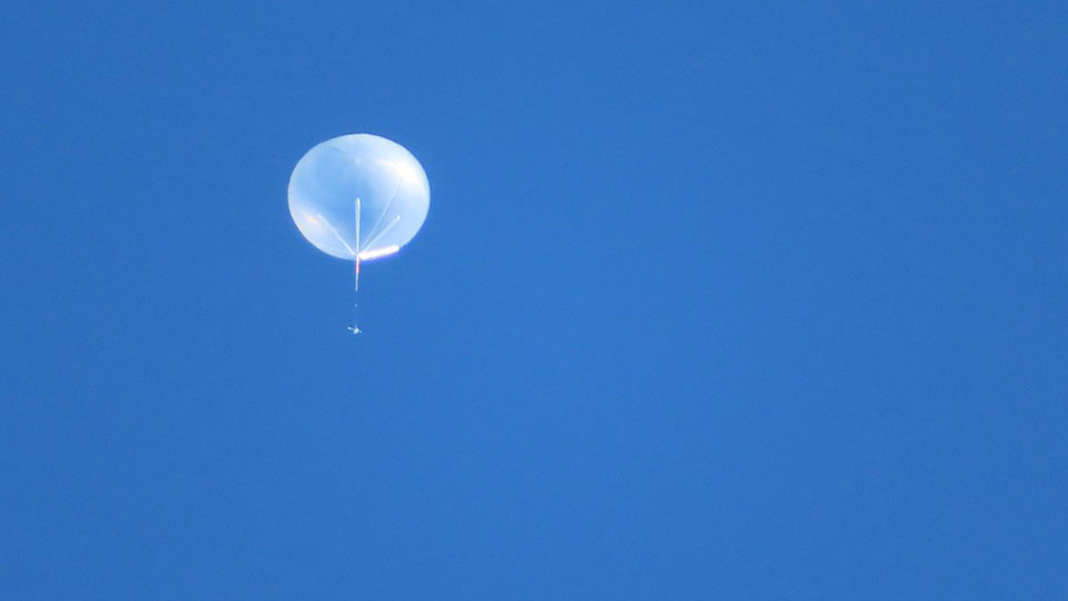 Large, translucent XL-Calibur balloon floating in a blue sky