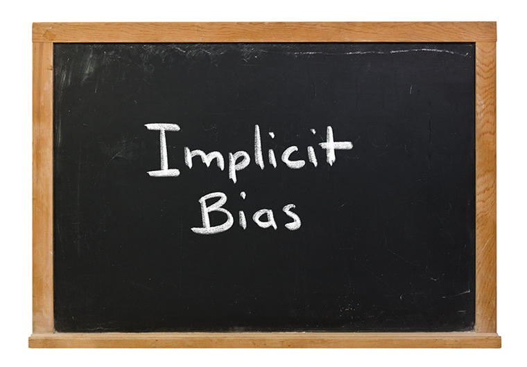 Implicit Bias written in white chalk on a black chalkboard isolated on white