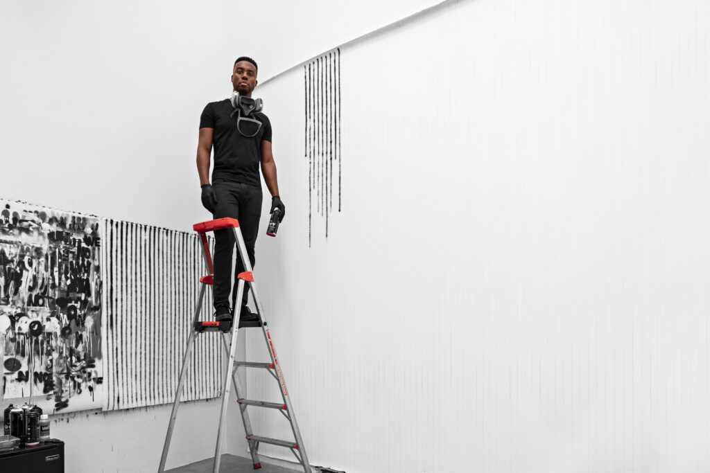 Artist Adam Pendleton stands on a ladder in his studio.