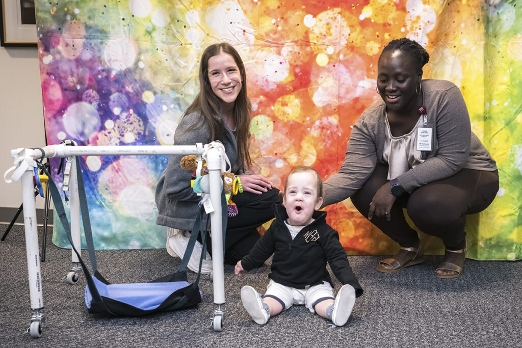 students pose with an assistive tech device and the small baby who will use it
