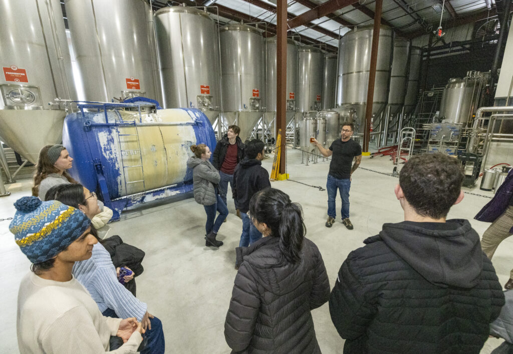 Kurt Driesner points to fermenting tanks while a group of students looks on.